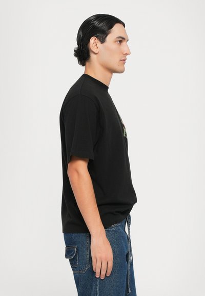 Black cotton t-shirt with a round neck, short sleeves, and a side view. Paired with blue denim pants featuring a pocket detail.