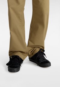 Sneaker nere con tomaie in suede e canvas, dotate di lacci tondi e una suola in gomma testurizzata, abbinate a pantaloni khaki.