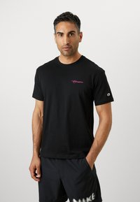 Schwarzes Baumwoll-T-Shirt mit Rundhalsausschnitt, kurzen Ärmeln und pinkem "Champion"-Logo auf der linken Brust. Hat eine klassische Passform und eine weiche Textur.