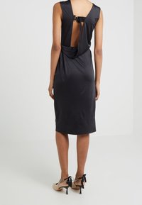 Vestido negro sin mangas con un respaldo drapeado, que presenta un acento de herrajes circular. Hecho de una tela suave, a la altura de la rodilla y con una silueta ajustada.