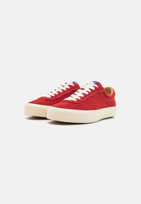 Red suede sneakers with white laces, round toe, and off-white rubber soles. Blue accents at the heel add detail to the design.