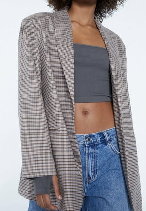 Donna che indossa un blazer oversize a quadri, top bandeau grigio e jeans blu a vita alta, mostrata dal collo ai fianchi su sfondo bianco.