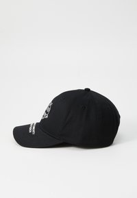 Black baseball cap with curved brim, embroidered logo on the front, and text on the side. Made of cotton, features ventilation holes.