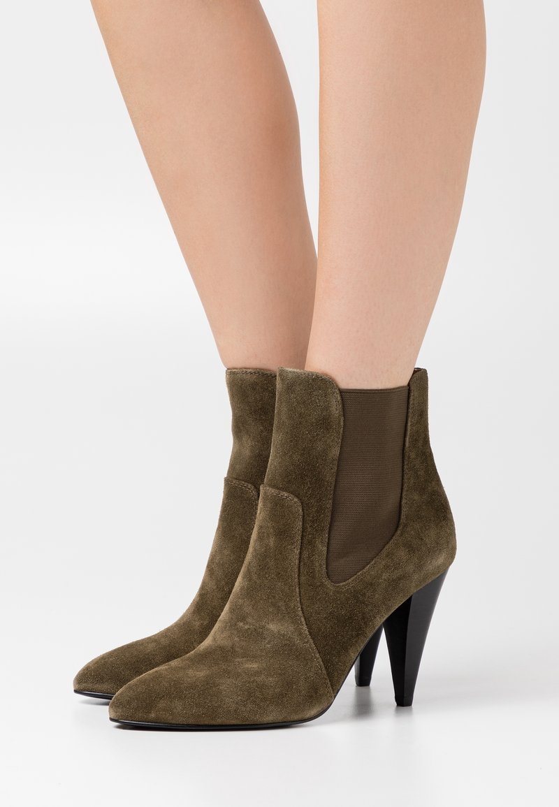 Bottines en daim vert olive avec bouts pointus, panneaux latéraux élastiques et talons aiguilles noirs. Texture lisse avec des accents minimaux.