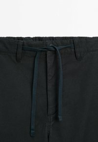 Zwarte broek met een elastische tailleband, voorzien van een blauwe koord. De stof heeft een licht gestructureerde afwerking en een ontspannen pasvorm.