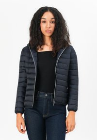 Marineblauwe pufferjack met een ritssluiting aan de voorkant, een aansluitend ontwerp, gestructureerde horizontale strepen en elastische manchetten. Draagt over een zwarte top en jeans.