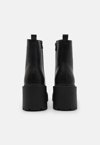 Botas de tobillo de cuero negro con una suela de plataforma gruesa, que presentan una textura suave y una cremallera en la parte posterior para facilitar su uso.