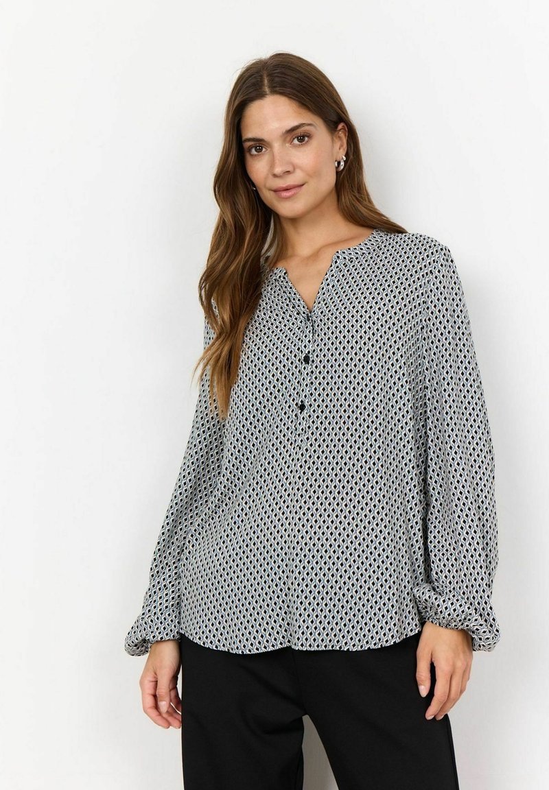 Blouse à motifs en tissu léger, présentant un design géométrique noir et blanc, avec une fermeture à bouton sur le devant et des manches longues avec des poignets élastiques.