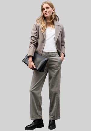 Grå uldblazer over en hvid skjorte, beige brede bukser med knapdetaljer og sorte læderankelstøvler. Holder en sort clutch-taske.