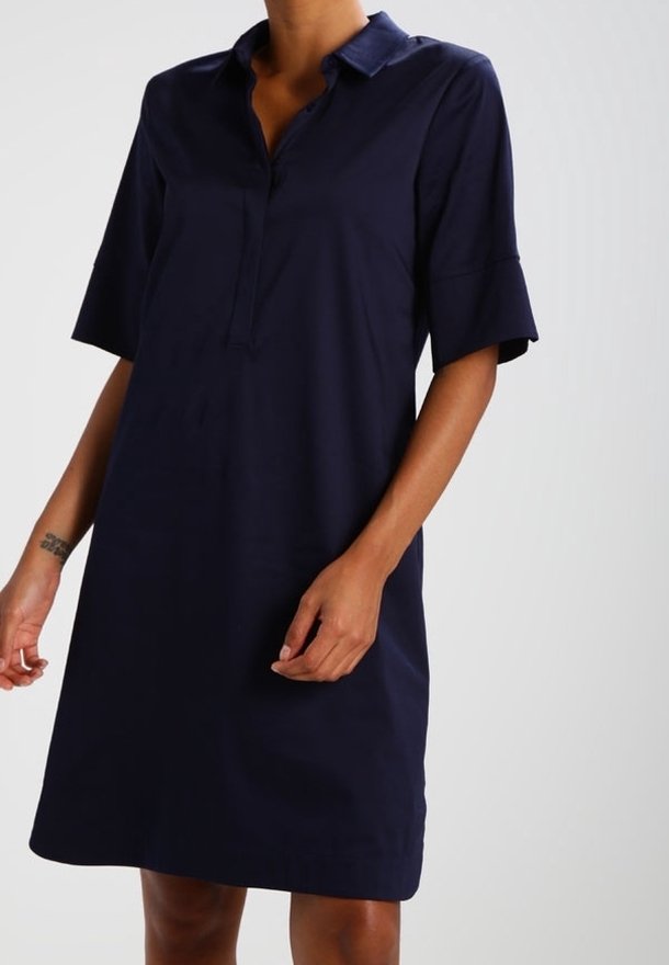 Mörkblå klänning med korta ärmar, krage, knappslå och avslappnad passform. Slät tyg med en subtil lyster och knälång nederdel.