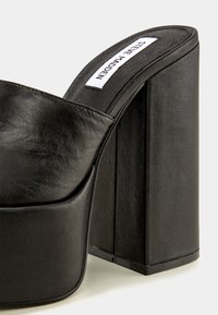 Mule plateforme noire avec un talon haut et épais et une tige en cuir, portant le nom de la marque Steve Madden à l'intérieur de la semelle.