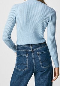 Pull en maille bleu clair avec des manches longues, associé à un jean en denim bleu foncé taille haute avec deux poches arrière et des coutures discrètes.