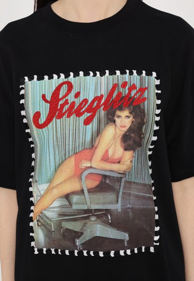 Camiseta negra con un gráfico vintage impreso de una mujer con un vestido rojo, bordeado con un patrón a rayas. Textura de tela suave.