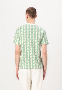 Tricou verde cu un model geometric pe un fundal deschis, cu mâneci scurte și guler rotund. Textură din bumbac, croială lejeră.