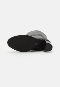 Cizmă din piele neagră, până la genunchi, cu detalii cusute, vârf rotunjit și talpă plată din cauciuc, evidențiind o textură netedă și un design minimalist.