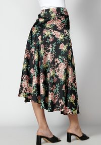 Knee-length skirt dengan pola bunga berwarna merah muda dan hijau di latar belakang hitam, terbuat dari bahan halus, memiliki hem yang mengalir dan pinggang elastis.