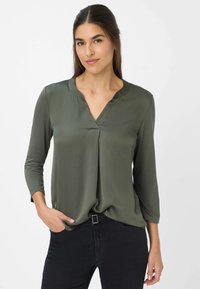 Oliven grøn bluse med V-hals og trekvartærmer, lavet af et glat materiale, med en plissering i midten for ekstra design.