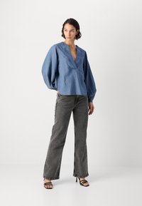 Blå denimskjorte med dyp V-hals og puffermer, kombinert med høyt liv grå jeans og svarte stroppesandaler.