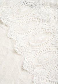 White lace fabric featuring intricate pattern with oval motifs. Textured edges with fine detailing and a soft, smooth background.