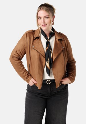 Bruine faux suede motorjack met een afgeplat kraag, zijritsen en zwarte accenten, gecombineerd met een wit bovenstuk en een geprint sjaaltje.