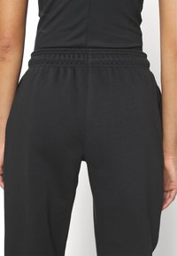 Svarta sweatsbyxor i mjukt tyg, med elastisk midja och sidfickor. Slät textur med avslappnad passform och avsmalnande ben.