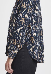 Blusa navy con stampa animale mista in tonalità di beige e bianco, in tessuto leggero, con maniche lunghe e un design a orlo alto-basso.