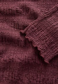 Primo piano di tessuto strutturato color malva scuro con superficie arricciata e piegata con piccoli volant.