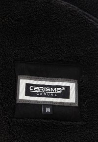 Juodos spalvos vilnos audinys su tekstūruota išvaizda. Ant audinio yra etiketė su užrašu „CARISMA CASUAL“ ir dydžio žymė „M“ apačioje.