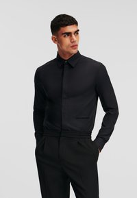 Schwarzes Langarmhemd mit Kentkragen, glatter Textur und subtiler Sheen; mit Karl Lagerfeld Logo nahe dem Saum.