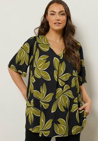 Tunique noire avec des motifs de feuilles vertes, à manches courtes, col en V et poches, fabriquée à partir d'un tissu texturé.
