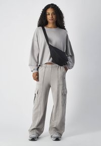 Grijze oversized sweatshirt met een losse pasvorm, gecombineerd met lichtgrijze cargobroek met zijzakken en een zwarte crossbody tas.