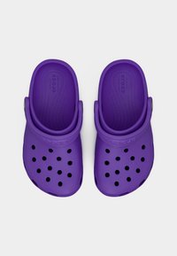 Ζευγάρι μωβ Crocs σανδάλια με λουράκια στο πίσω μέρος και οπές αερισμού, εμφανιζόμενα από πάνω σε λευκό φόντο.