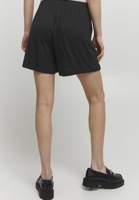 Svarta shorts i mjukt tyg med elastisk midja. Har en rak skärning och en enkel design, parat med svarta slip-on skor.