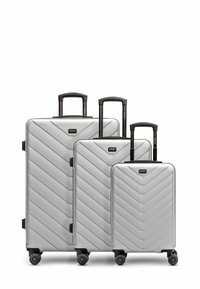 Trois valises empilées en argent avec un motif en chevrons, dotées de poignées télescopiques et de quatre roues pour une mobilité aisée.