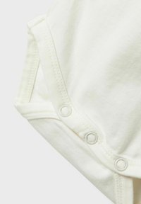 Body in cotone color crema con chiusure a scatto sul fondo e cuciture piatte, caratterizzato da una consistenza morbida e un design semplice.