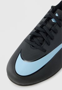 Musta urheilukenkä, jossa on sileä, teksturoidulla pinnalla, sininen swoosh-yksityiskohta ja mustat nauhat. Pyöreä kärki ja tyylikäs muotoilu.