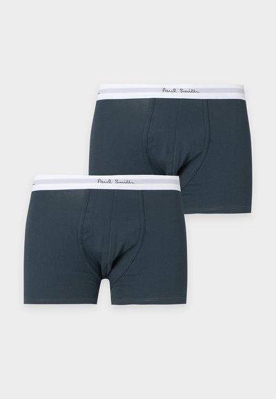 Deux boxers gris foncé avec des ceintures élastiques blanches portant le logo Paul Smith sur un fond gris clair.