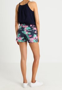 Débardeur bleu marine, shorts à motifs floraux avec des accents verts et roses, et baskets blanches. Les shorts ont une taille élastique et une coupe décontractée.