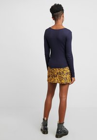 Top de manga larga en color azul marino combinado con una mini falda de estampado de serpiente amarillo. La modelo lleva botas negras con cordones, que muestran un diseño de tela texturizada.