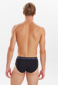 Sorte herreunderbukser med en elastisk talje, der har grå bogstaver, glat stof og en tætsiddende design, set bagfra.