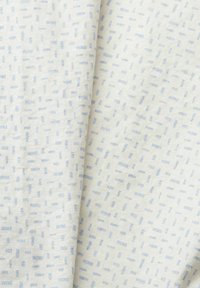 Gros plan d’un tissu blanc avec de petites lignes bleues en pointillés disposées aléatoirement, montrant la texture et des plis légers.