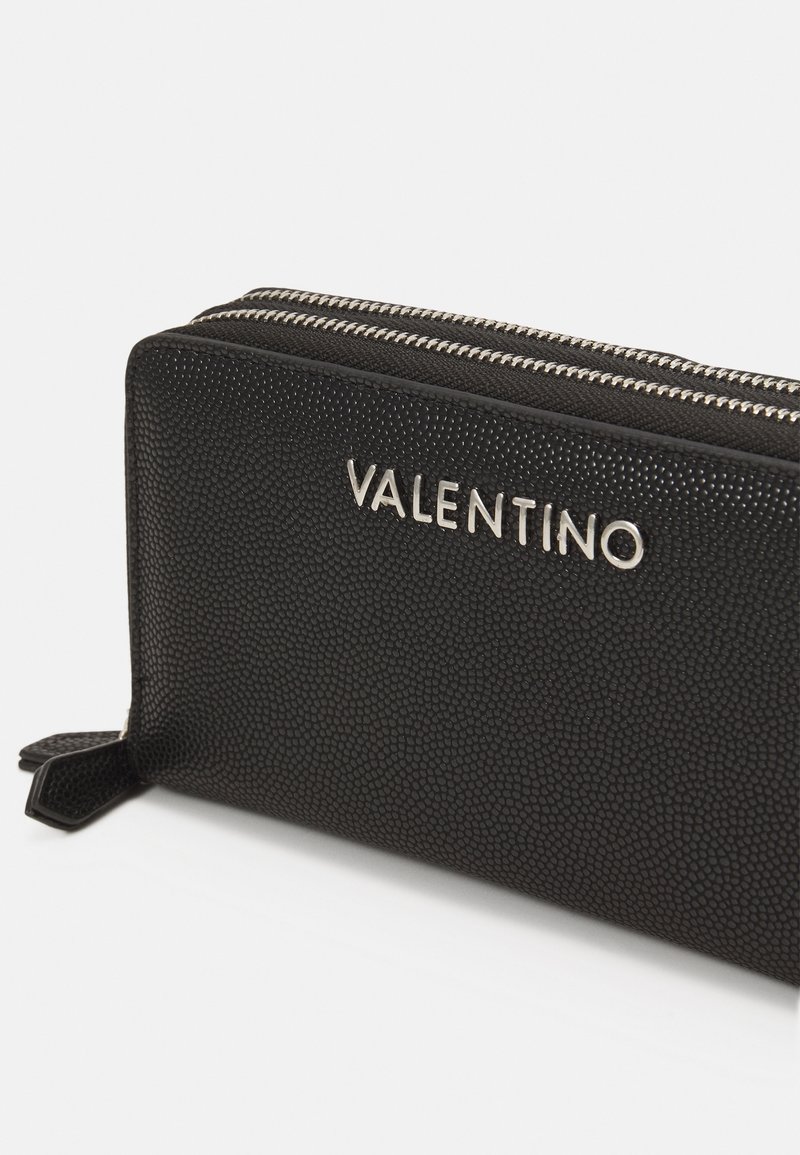 Schwarze Lederbörse mit strukturiertem Äußeren, ausgestattet mit einem silbernen "VALENTINO"-Logo und zwei metallic glänzenden Reißverschlüssen zum Schließen.