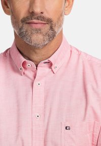 Lichtroze button-up overhemd met een kraag, contrasterende witte knopen en een zakje met een geborduurd logo op de borst.