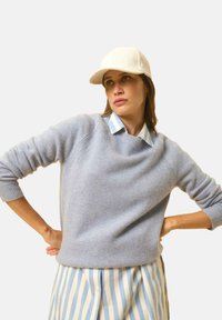 Lichtblauwe trui van zacht materiaal, met een ronde halslijn en geribbelde manchetten. Draag hem over een blauw-wit gestreepte overhemd met kraag en een crèmekleurige pet.