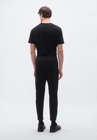 Czarny t-shirt z krótkim rękawem oraz dopasowane spodnie dresowe z mankietami przy kostkach. Miękka tkanina, minimalistyczny design i sznurek ściągający w pasie, widok od tyłu.