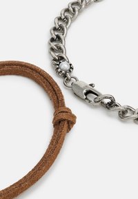 Culoare maro, cordon din suede, cu o curea din argint, prezentând un închizător tip lobster și un accent de perlă, evidențiind o combinație de texturi și strălucire metalică.