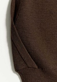 Gros plan d'un tissu tricoté marron avec un bord plié et des coutures visibles sur un fond clair.