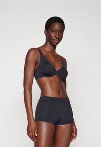 Black seamless bra with adjustable straps and molded cups, paired with matching black hipster shorts, smooth texture, no visible patterns.