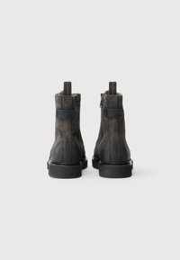 Bottes cheville en daim noir avec fermetures éclair latérales, languettes de tirage et panneaux texturés sur la tige. Semelles épaisses en caoutchouc. Vue de dos.