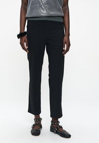 Schwarze Cargo-Hosen mit schlanker Passform, die seitliche Taschen und eine glatte Textur aufweisen. Kombiniert mit schwarzen Riemenschuhen und einem Paillettenoberteil.